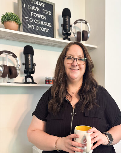 Marketing strategist smiling with coffee mug in hand in front of podcast setup. 