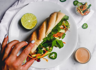 An image of a baguette with greens, cilantros, and carrots coming out of it and a hand grabbing it.