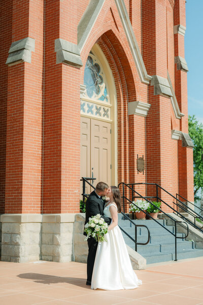 bride and groom share a kiss in front of church steps