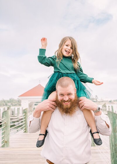 Little girl on his Dad's shoulders laughing and playing