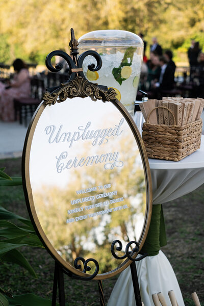 Ornate gold oval mirror with calligraphy writing displayed on easel at outdoor wedding