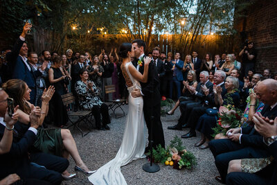 Photo from far away of bride and groom standing together while man gives speech on the dance floor