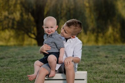 two brothers sitting on white box with baby on lap
