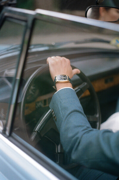 Groom in navy suit with watch driving a vintage car