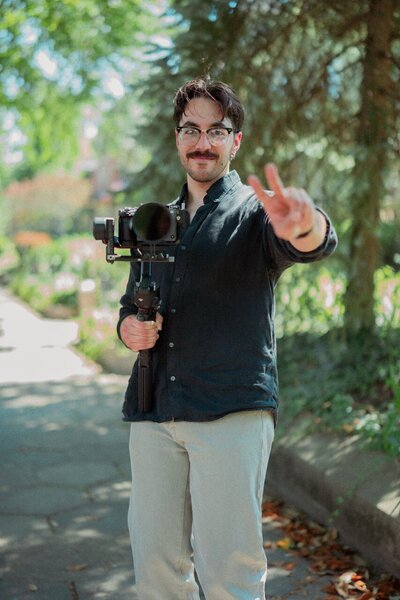 Informal headshot of Louisville wedding videographer Reventure Media holding up a camera and putting up a peace sign.