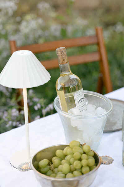 Outdoor table with wine, grapes, and a vintage lamp styled for a countryside picnic — Dani Lacey Photographs in Greenville SC.