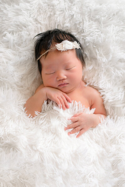 Newborn baby girl sleeping on a white fuzzy blanket with her hand tucked under her chin
