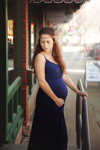 Pregnant woman in blue dress smiling with eyes closed.