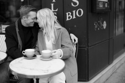 black and white image of a couple sitting at a cafe in paris with their foreheads together