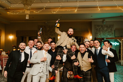 Group of men pose holding groom up on their shoulders on dancefloor during wedding at maryculter house hotel