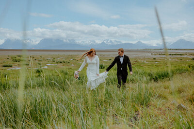 bride and groom walking through a field of grass