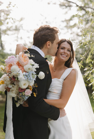 Groom kissing bride's cheek during sunset photos at Camelot manor