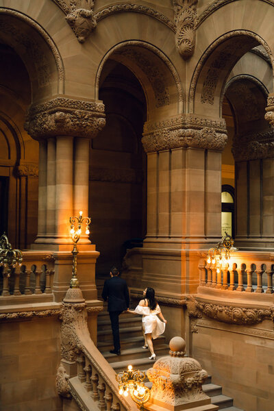 Engagement photo session in an Saratoga Springs, New York building with classic architecture, winding staircases, and warm, yellow lighting.