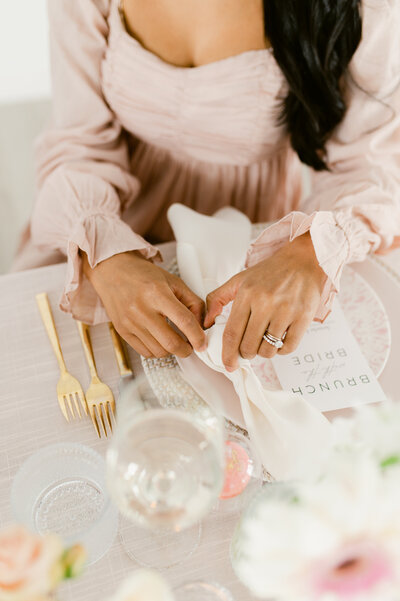 A woman places a white napkin on a pink bridal shower table setting.