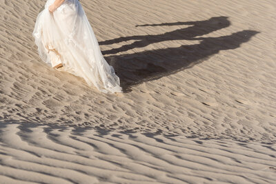 A person in a wedding dress walking up a sand dune
