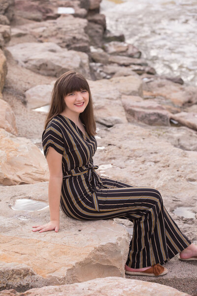 senior-girl-in-stripped-jump-suit-sitting-on-rocks-in-fort-wroth-tx-park