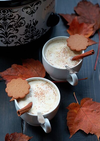 two mugs of hot chocolate with cookies and cinnamon sticks sitting on a blue table with leaves