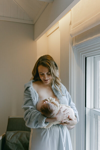 A mother breastfeeding her baby by the hotel window