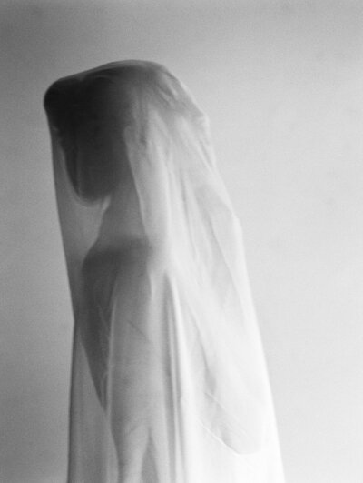 Black and white off beat wedding photo of a bride thowing her gown over her head to seem like she is floating in the clouds or falling from the sky.