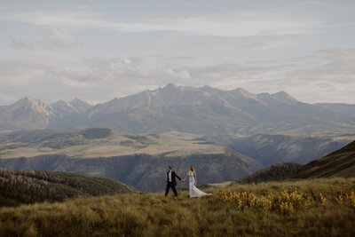 Bride and groom hold hands as they walk through the mountains on their elopement day.