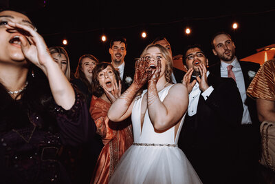 A bride wearing traditional henna cheers along with her guests at her wedding reception