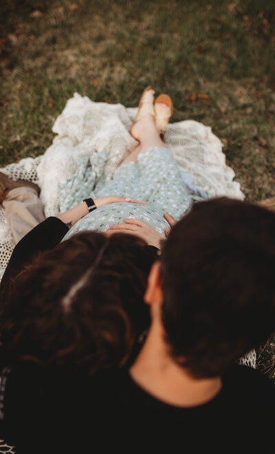 A couple hold each other in a field touching mom's pregnant stomach in Blacksburg, Virginia.