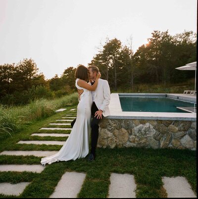 The bride and groom pose happily by a serene pool, capturing a joyful moment on their wedding day.