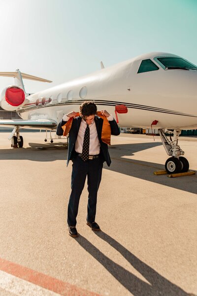 Male graduate adjusting stole in front of an airplane.