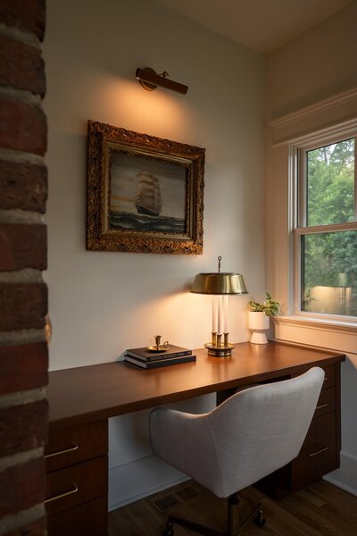 Colonial-style renovated home with modern eclectic built-in desk nook, cozy and museum lighting, exposed brick wall, and artwork display.