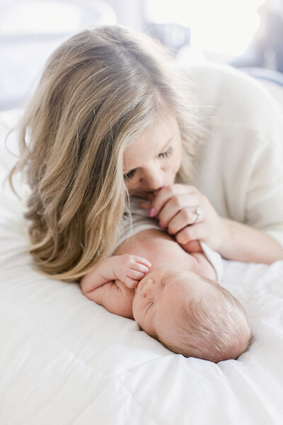 Mother kissing newborn's hand while laying on bed.