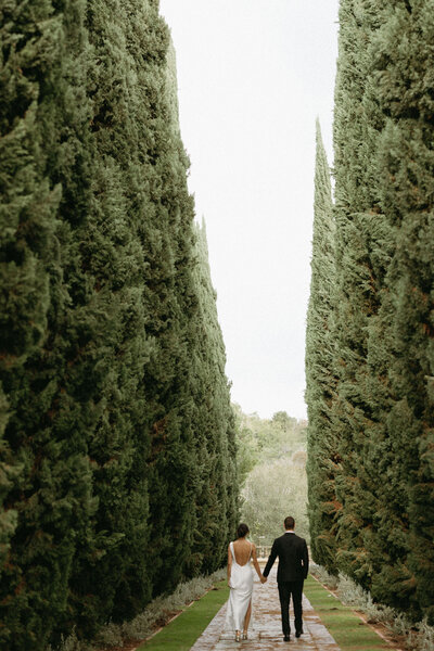 Beverly Hills Couples Session. Couple in cocktail attire standing together holding hands between tall green hedges