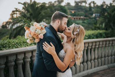 Wedding couple at The Greystone Mansion in California. Bride has a beautiful lace gown while groom has  an elegant tuxedo.  Bride is holding a beautiful blush lush bridal bouquet in her hand.