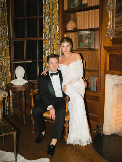 Flash photo of room sitting in a chair with bride sitting on the arm of the chair in front of wooden shelves
