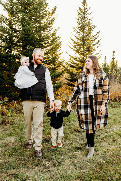 beautiful family with two little kids walking in front of the Christmas trees captured by Ashley Kalbus