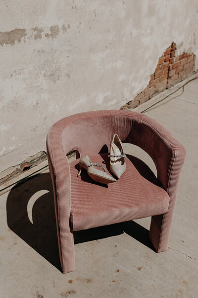 Jimmy Choo shoes sit on pastel pink lounge chair