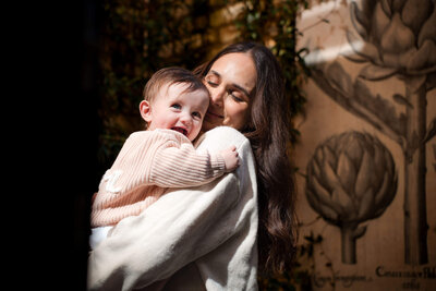 A tender embrace between parent and child in soft lighting against a decorative wall with floral patterns.