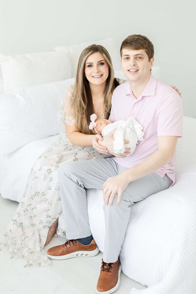 Mother and Father sitting on bed holding baby during newborn photography session in Dothan Alabama Photography Studio