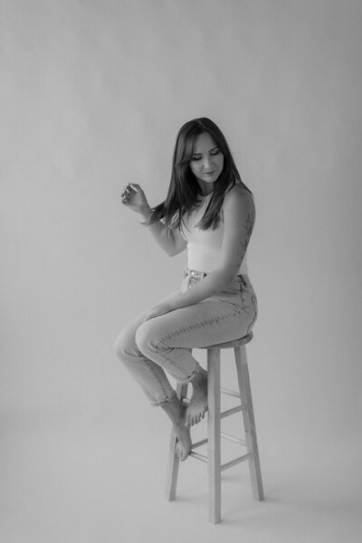 A person sitting on a stool looking down to the side 