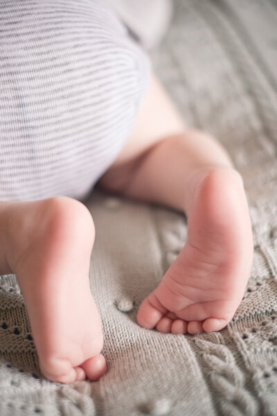 Die kleinen nackten Füße eines Babys, das auf dem Bauch auf einer Wolldecke liegt, werden in einer Nahaufnahme gezeigt.