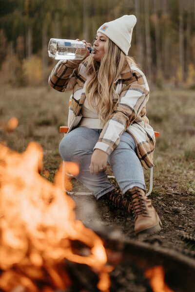 woman sitting next to a campfire and drinking
