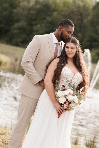 Bride in white dress and floral bouquet standing next to white wedding venue