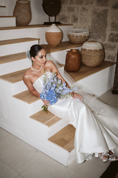 Bride sitting on staircase with blue floral bouquet