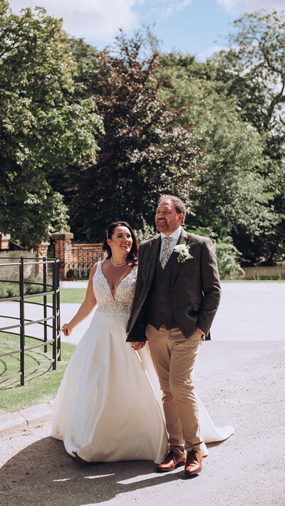 Bride and groom walking beside field at Manor Barn in Cambridge