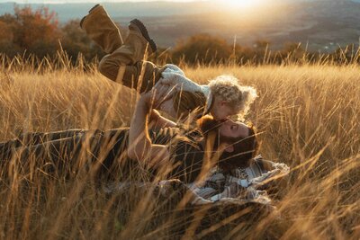 Dad playing airplane with his toddler son brings him in for a kiss while the sun sets behind them.