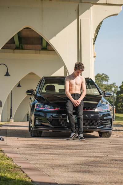 Male shirtless posed with his car, under an underpass in South Carolina.