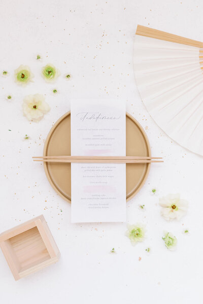 Japanese wedding menu styled with chopsticks, a hand fan, and a masu — elegant accents for kimono wedding rental in Los Angeles, California | お箸・扇子・枡でスタイリングした和のウェディングメニュー。ロサンゼルス（カリフォルニア）の着物ウェディングレンタル向けの上品なアクセント