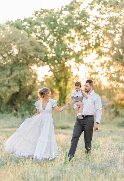 A family of four stand in a field of purple lupines dressed in shades of grey, blue, and white while smiling and holding one another photographed by bay area photographer, Light Livin Photography.