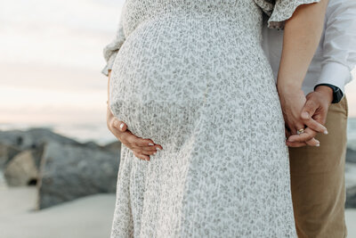 Maternity Portrait taken at Vilano Beach near Jacksonville with the mother in a blue patterned dress while her husband laces fingers with her