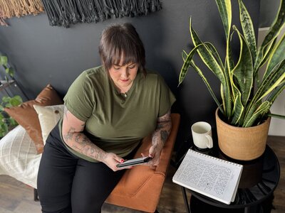 Website designer of AQ Design Studio taking a break to sit on the couch with a cup of coffee and read a book on her kindle