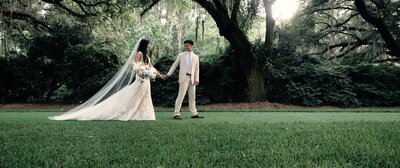 A newlywed couple holding hands and walking in a field 
